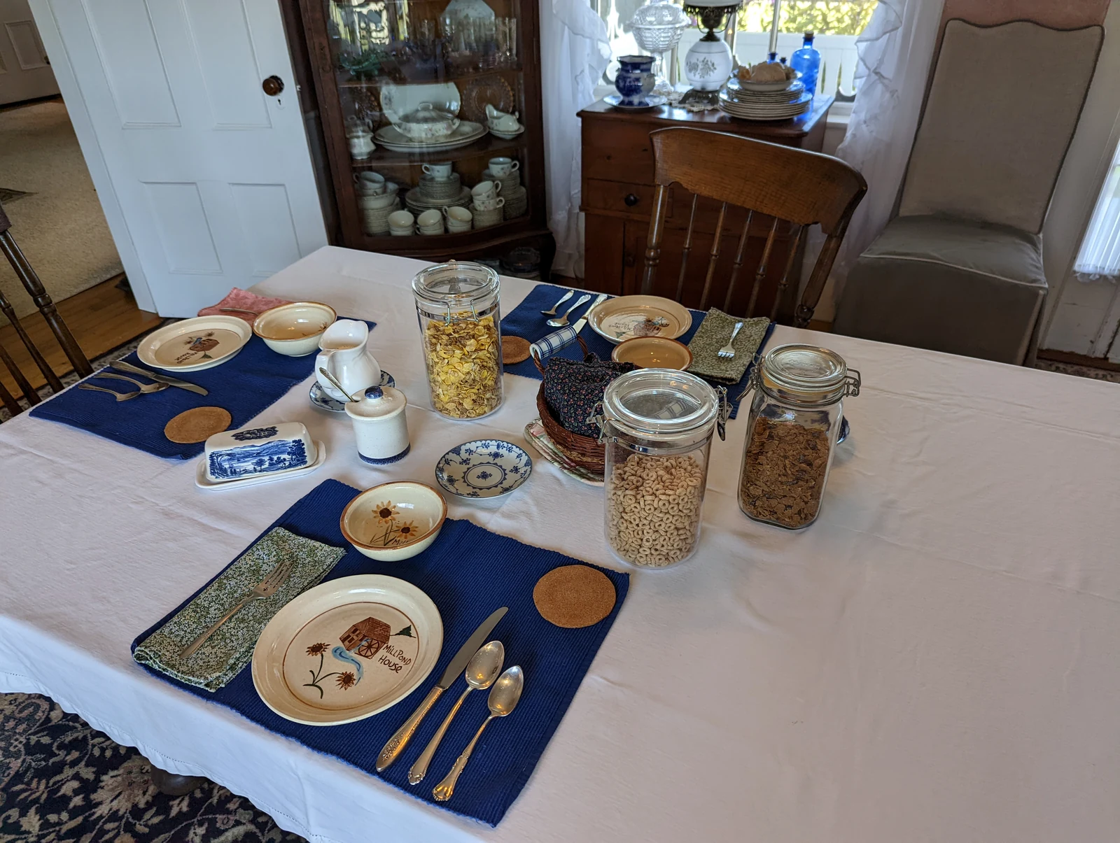 The dining room table laid for breakfast, with cereal in glass jars, a blue transferware butter dish, and the hand-painted Mill Pond House plates