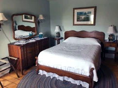 A guest room with a carved wooden headboard, a white candlewick spread and a dresser with a swing mirror