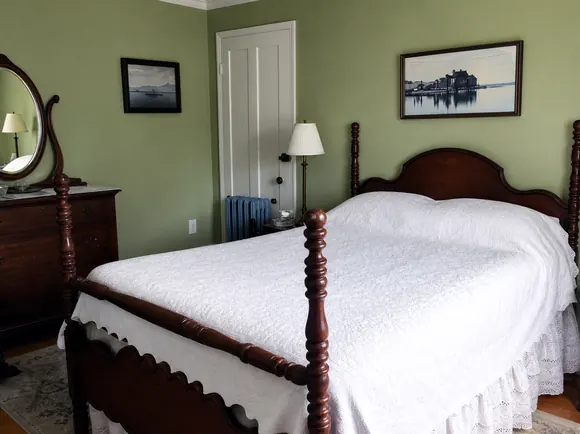 A guest room with sage-green walls, a spool bed with a white spread and a washstand