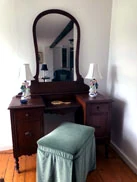 A vanity table with a shield mirror and a skirted stool